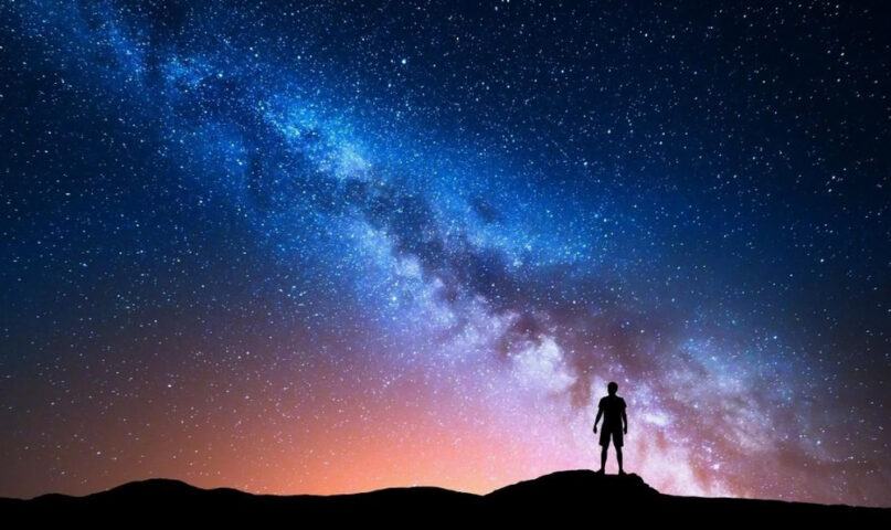 God is not angry at you — silhouette of a person beneath the Milky Way and a glowing night sky